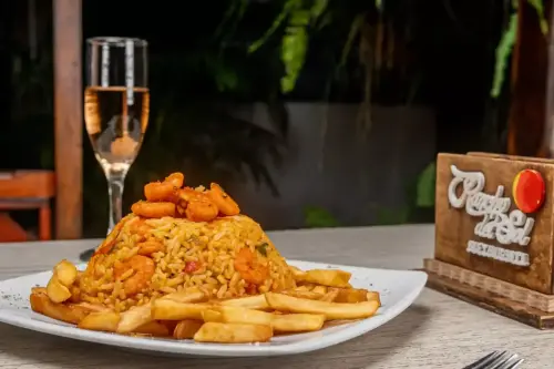 Plato de arroz con camarones acompañado de papas fritas, servido en el restaurante Rancho del Sol con una copa de vino espumoso.