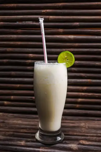 Limonada de coco servida en vaso alto con rodaja de limón y pitillo, sobre fondo rústico de madera.