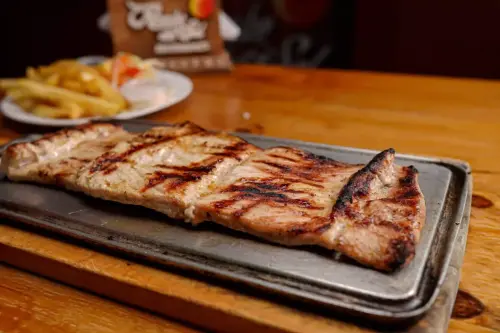 Lomo de cerdo a la parrilla servida en una plancha caliente, acompañada de papas fritas y ensalada en el restaurante Rancho del Sol.