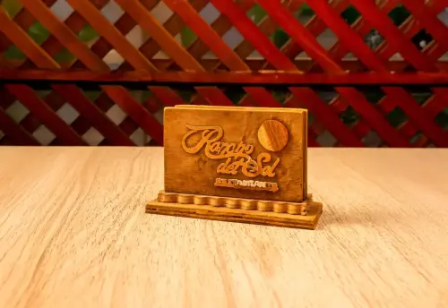 Porta servilletas de madera con el nombre y logo del restaurante Rancho del Sol, colocado sobre una mesa de madera en un entorno rústico.